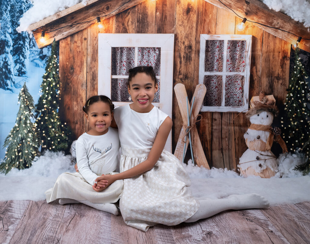 deux sœurs assises devant un chalet des neiges Mini-séance de Noël Houilles Yvelines photographe famille Houilles photographe famille Yvelines photographe famille Hauts-de-Seine photographe famille Ile-de-France